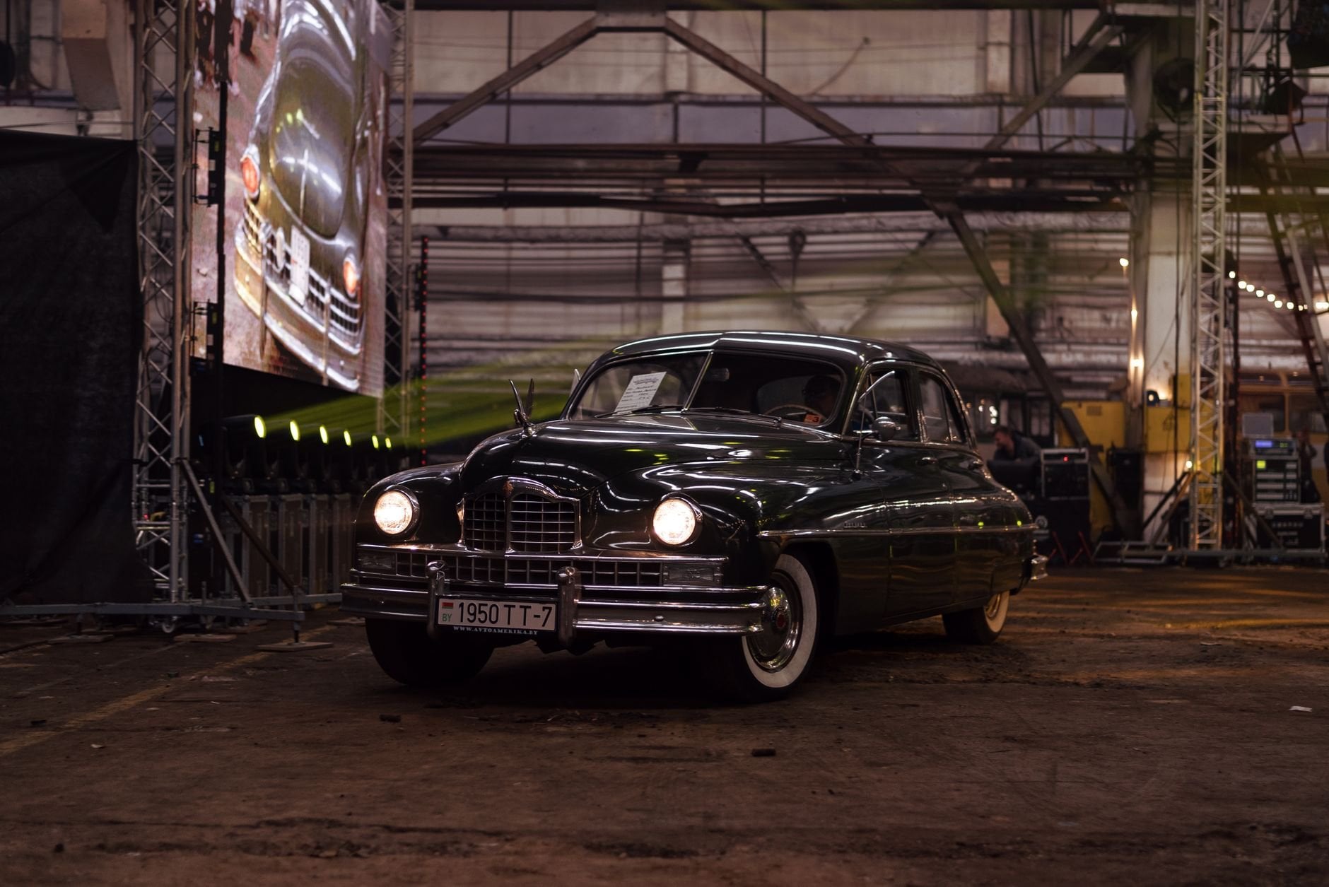 Classic black vintage car on display in a dimly lit industrial environment.